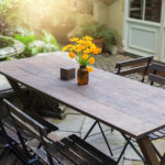 Dining wooden table in the outdoor garden decorated with yellow flower vases.