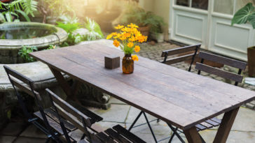 Dining wooden table in the outdoor garden decorated with yellow flower vases.