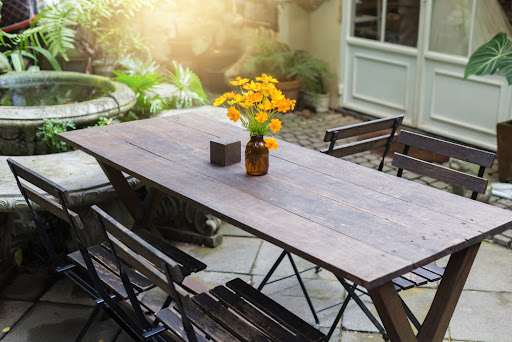 Dining wooden table in the outdoor garden decorated with yellow flower vases.