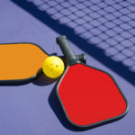Pickleball - 2 Paddles and A Ball Lying on Court Near Net Shadow