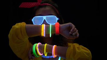 Cheerful young woman with neon bracelets in dark room