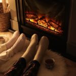 Couple-wearing-knit-socks-seated-on-furry-rug-and-stretching-their-legs-in-front-of-fireplace