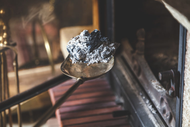 Scooping-ash-and-charred-wood-out-of-fireplace-with-metal-shovel.