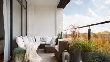 Outdoor-balcony-with-cushioned-rattan-furniture-green-plants-and-glass-railing.