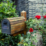 Rustic-wooden-mailbox-surrounded-by-green-plants-and-red-roses.
