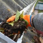 Person wearing gardening gloves pulling debris out of gutter