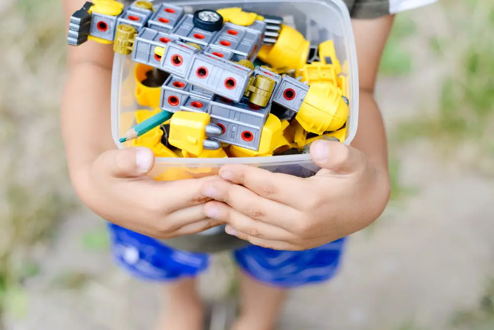 Child holding bin of toys outdoors