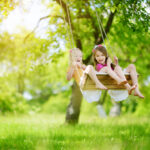 Two-young-girls-smiling-while-swinging-on-wooden-tree-swing